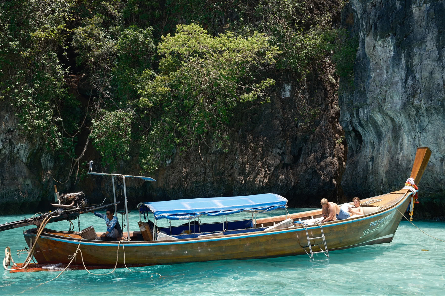 Longtail boat with passengers in clear blue water near a rocky cliff